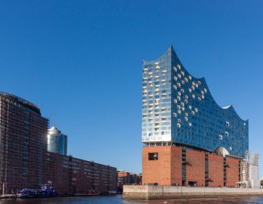 HAMBURG, GERMANY - 12 AĞUSTOS 2024: Elbphilharmonie konser salonunun çarpıcı modern mimarisi Hamburg 'daki tarihi tuğla depo binasının yanında duruyor