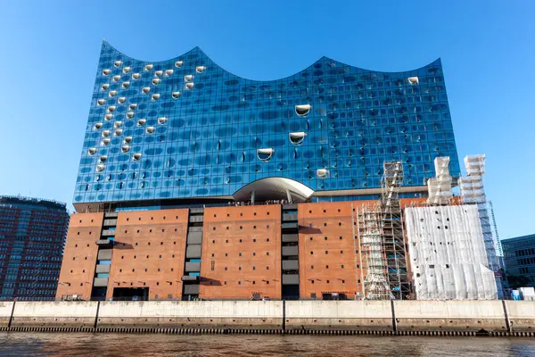 HAMBURG, GERMANY - 12 AĞUSTOS 2024: Hamburg 'daki sembolik Elbphilharmonie konser salonunun düşük açılı görüntüsü, etkileyici cam cephesini ve tuğla taban görüntüsünü gözler önüne seriyor