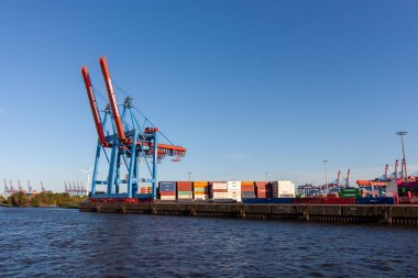 HAMBURG, GERMANY - 12 Ağustos 2024: Hamburg 'daki büyük bir konteyner terminalinin geniş açılı görüntüsü, liman boyunca büyük mavi ve kırmızı vinçler ve nakliye konteynırları sergileniyor