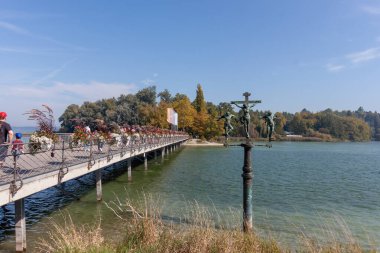 KONSTANZ, MAINAU - SEPTEMBER 21, 2025: A unique bronze sculpture of the crucifixion stands near the flower-adorned bridge leading to Mainau Island on Lake Constance