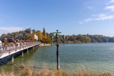 KONSTANZ, MAINAU - SEPTEMBER 21, 2025: A unique bronze sculpture of the crucifixion stands near the flower-adorned bridge leading to Mainau Island on Lake Constance