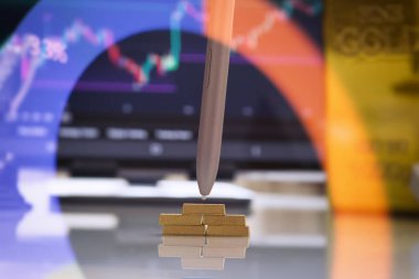 Stylus, servetin planlanması ve değerli metal yatırımını temsil eden, borsa grafikleri ve finansal veri örtüleriyle altın külçelerini işaret ediyor.