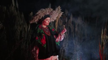 Ukraynalı bir kadın elinde mumla bataklıkta yürüyen bir cadı gibi, geceleri dışarıda geleneksel bir kostümle dolaşıyor. Ukrayna 'nın gizemi, etnik kıyafetler, sihir. Yüksek kalite 4k görüntü