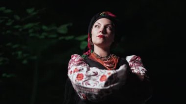 Geleneksel Ukrayna mendili, kolye ve gece ormanı arka planında kostümlü güzel bir kadın. Ulusal giysili kadın - vyshyvanka, antik mercan boncukları. Etnik tarz kavramı, gelenekler. 4k
