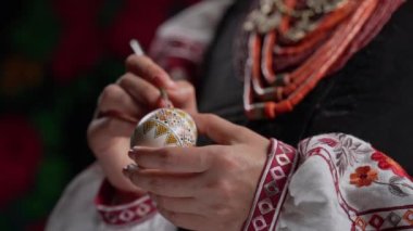 Paskalya yumurtasına geleneksel orisim çizen Ukraynalı kadın: Pysanka. Ulusal kostümle çalışan bir sanatçı. Hristiyan bayramı için hazırlık. Yüksek kalite 4k görüntü
