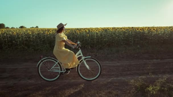 在向日葵地附近的乡间路上 身着长裙的农村妇女独自骑着复古风格的白色自行车 老式时尚 惊人的冒险 乡村活动 健康的生活方式 高品质4K — 图库视频影像
