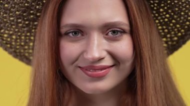 Renkli sarı stüdyo arka planında çekici kadın hasır şapka. Avrupa görünümlü gülümseyen olumlu bayan kameraya bakıyor. Yaz, tatil, seyahat konsepti. Yüksek kalite 4k görüntü