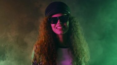 Neon renkli ışıkta dans eden modaya uygun bir kadın. Dumanlı arka plan, gece partisi, disko kulübü. Z jenerasyonu esrarengiz Afro-Amerikan kadın Panama şapkalı, gözlüklü. Yüksek kalite 4k görüntü