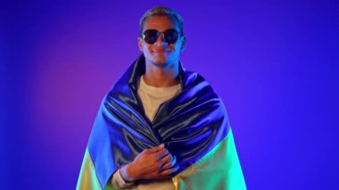 Ulusal Ukrayna bayrağıyla gülümseyen adam. Ukrayna, vatansever, savaş kutlamalarında zafer, bayrak, Bağımsızlık Günü. Neon çok renkli ışık. Yüksek kalite 4k görüntü