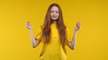 Sakin bir kadın dinleniyor, meditasyon yapıyor, stresi reddediyor. Güneşli kız derin derin nefes alıyor, sarı stüdyo arka planını sakinleştiriyor. Yoga, ahlaki denge, zen konsepti. Yüksek kalite 4k görüntü