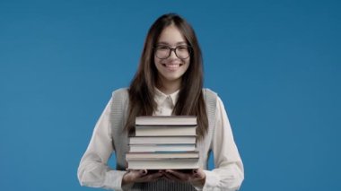 Asyalı gülümseyen öğrenci mavi arka planda üniversite kütüphanesinden bir yığın kitap tutuyor. Mutlu kız gülümser, mezun olduğu için mutludur. Yüksek kalite 4k görüntü