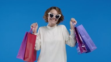 Satış sonrası kese kağıdıyla gezen neşeli kadın, siyah cuma indirimi, alışveriş koliği, mavi stüdyo geçmişi. Satın almanın tadını çıkaran genç bir alıcı. Yüksek kalite 4k görüntü