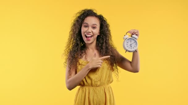 Mujer Rizada Feliz Con Reloj Despertador Sobre Fondo Amarillo Cálido — Vídeos de Stock