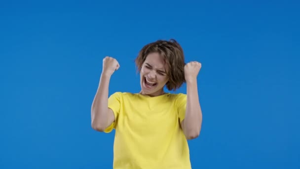 美しい女性は勝利のイエスジェスチャーを示しています 彼女は結果を達成しました 女の子 幸せな 青の背景に興奮した幸せな女性を驚かせた ジャックポットのコンセプト 高品質4K映像 — ストック動画