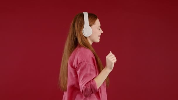 赤いスタジオをバックにヘッドフォンでダンスを楽しむ 美しい女性が音楽を聴いています ラジオ 無線近代的なサウンド技術 オンラインプレーヤー 高品質4K映像 — ストック動画