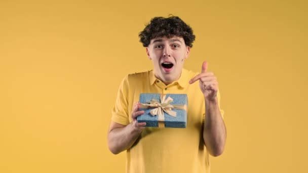 興奮した男は弓でギフトボックスを保持します 彼は喜んで注目している 男は黄色の背景にプレゼントと笑顔 スタジオ ポートレート 高品質4K映像 — ストック動画