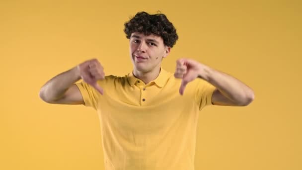 親指の下のジェスチャー 黄色の背景を示すことに不満を表明若い千年紀の男 嫌いの印を持つ男の肖像画 高品質4K映像 — ストック動画