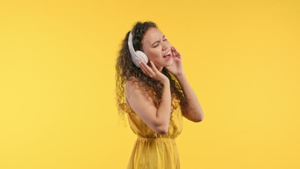 美丽的夏季女子听着音乐 喜欢在黄色工作室的背景下与耳机共舞 无线电 无线现代音响技术 在线播放器 高质量的4K镜头 — 图库视频影像