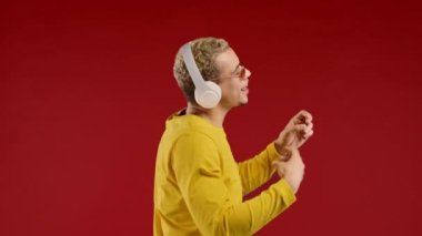 Pozitif Amerikalı Afrikalı müzik dinleyen, kırmızı stüdyo arka planında kulaklıkla dans eden bir adam. Radyo, kablosuz modern ses teknolojisi, çevrimiçi çalar. Yüksek kalite 4k görüntü