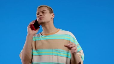 Karizmatik bir adam arkadaşıyla telefonla konuşur, uzaktan iletişim kurar, güzel şakalar yapar, mavi arka planda güler. Telefon görüşmesi. Yüksek kalite 4k görüntü