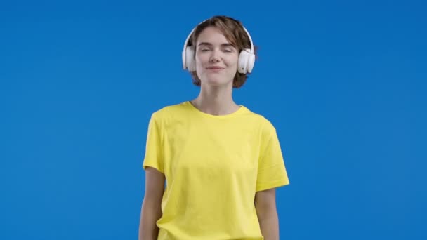 漂亮的女人听着音乐 喜欢在蓝色工作室背景下与耳机共舞 无线电 无线现代音响技术 在线播放器 高质量的4K镜头 — 图库视频影像