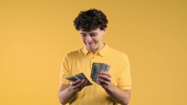 Amerikan doları sayan memnun bir adam. Genç milenyum çocuğu ya da öğrenci para sayıyor. Sarı duvarda dolar banknotları. Başarının, kazancın, maaşın, faydanın, yatırımların sembolü. Yüksek kalite 4k görüntü