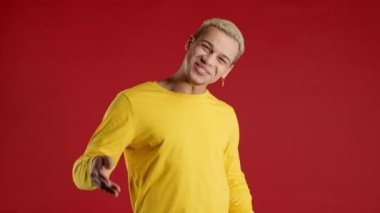 Adam ona katılmayı teklif eder, el sıkışma hareketi ile çağırır. Genç adam arıyor - Hey sen, buraya gel. Hippi ergen, şakacı, davetkar. Kırmızı stüdyo geçmişi. Yüksek kalite 4k görüntü