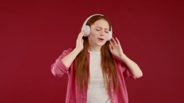 Pozitif Avrupalı kadın müzik dinliyor, kırmızı stüdyo arka planında kulaklıklarla dans etmekten hoşlanıyor. Radyo, kablosuz modern ses teknolojisi, çevrimiçi çalar. Yüksek kalite 4k görüntü
