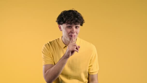 Shh ゴシップの概念のジェスチャーでハンサムな男 笑顔の男が唇に指を保持 黄色のスタジオの背景 そうだ 高品質4K映像 — ストック動画