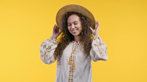 黄色のスタジオの背景にカメラに笑みを浮かべているウクライナ人の女性をいちゃつく かわいい流行の女の子は彼女のわらの帽子 夏のVyshyvankaの服を修正します 高品質4K映像 — ストック動画