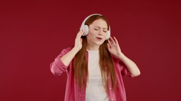 積極的なヨーロッパの女性は音楽を聞いて 赤いスタジオの背景にヘッドフォンでダンスを楽しんでいます ラジオ 無線近代的なサウンド技術 オンラインプレーヤー 高品質4K映像 — ストック動画