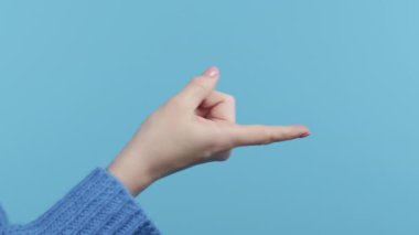 Tanımlanamayan bir kadın işaret veriyor. Mavi arka planda yakın çekim stüdyosu. Flört, baştan çıkarma konsepti. Yüksek kalite 4k görüntü