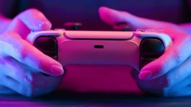 Oyuncuların elleri konsol TV 'de oyun oynuyor. Kumandalı, neon renkli ışık. Kadın düğmelere basıyor, kumanda kullanıyor, en yeni kablosuz oyun sahası. Hobi, e-spor, makro görüş. 4k görüntü