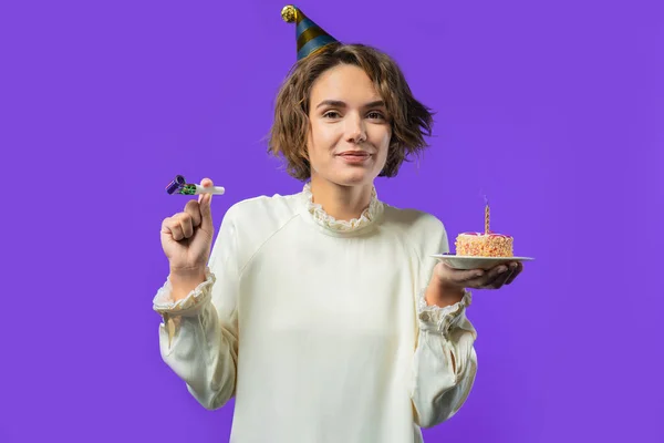 Happy birthday woman making wish - candle on cake. Girl smiling, celebrating anniversary. Young stylish lady on violet background. High quality photo