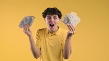 Nakit parası olan zengin, heyecanlı bir adam. Sarı duvardaki Amerikan doları banknotları. İkramiyenin, kazancın, zaferin, piyangoyu kazanmanın sembolü. Yüksek kalite 4k görüntü