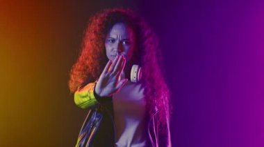 Kulaklıklı ciddi bir genç dur işareti ile reddedilme hareketi gösteriyor. Sinyal yeterli. Gradyan neon rengi arka planda bir bayan. Yüksek kalite 4k görüntü