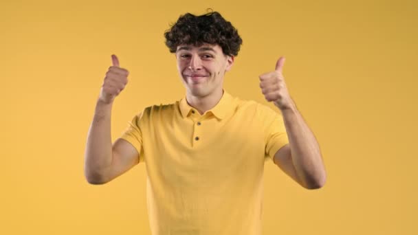 肯定的な巻き毛の男は 親指をジェスチャーのように手のサインを作る 黄色の幸せな学生の男 正しい完璧な選択 大きな取引 スタジオの背景 そうだ 高品質4K映像 — ストック動画