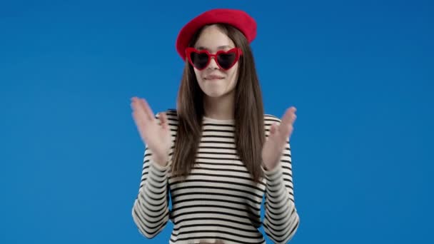 Snygg Kvinna Applåderar Blå Bakgrund Dam Röd Basker Och Glasögon — Stockvideo
