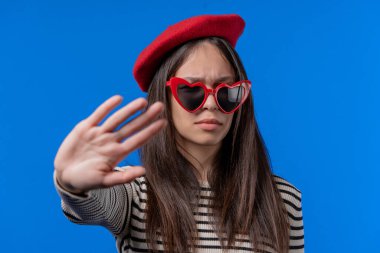 El işaretine hayır diyen ilgisiz bir kadın. İnkar etmek, reddetmek, katılmamak. Mavi arka planda kırmızı gözlüklü genç bayan portresi, mola kavramı. Yüksek kalite fotoğraf