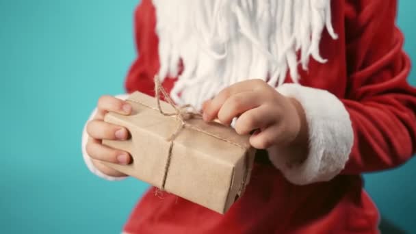 身穿圣诞老人服装的男孩手拉着一串包裹的礼品盒 孩子不知道里面是什么 快乐的孩子与礼物 蓝色的圣诞背景高质量的4K镜头 — 图库视频影像