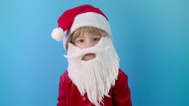 有趣的男孩穿着圣诞老人的服装与胡子点头 是的信号 正确的完美选择 很大程度上 蓝色的圣诞背景高质量的4K镜头 — 图库视频影像