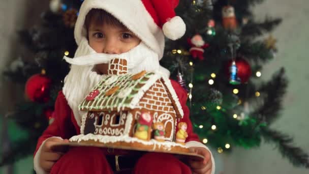 Cute Little Boy Stroju Świętego Mikołaja Siedzi Piernika Domu Tle — Wideo stockowe