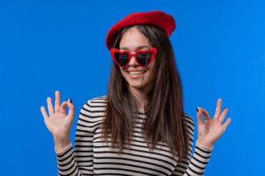 Güzel bir kadın el işareti yaptırır, tamam mı? Mutlu genç kız, doğru seçim, harika bir anlaşma, mavi özgeçmiş. Pozitif kadın model kameraya gülümser, onay, güven konsepti. Yüksek kalite fotoğraf