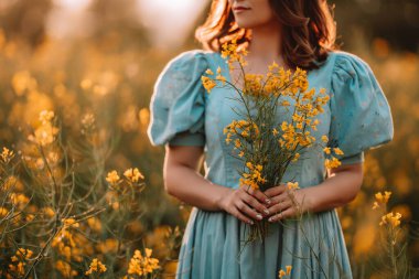 Çiçek tarlasında poz veren çekici bir kadının portresi. Hasır şapkalı, eski moda elbiseli zarif bir kız. Kolza tohumu çayırı, eski kıyafetler, bahar mevsimi.