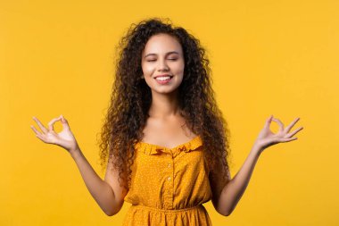 Sakin bir kadın dinleniyor, meditasyon yapıyor, stresi reddediyor. Güneşli kız derin derin nefes alıyor, sarı stüdyo arka planını sakinleştiriyor. Yoga, ahlaki denge, zen konsepti. Yüksek kalite fotoğraf