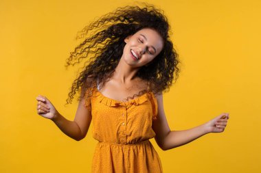 Woman dancing with big afro curly hair on yellow backdrop, hairstyle flying air. High quality photo