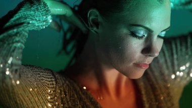 Beautiful woman posing in pool water under neon color light. Party, attractive chic in shining dress enjoying night time. Rich lifestyle, luxury life, influential people. High quality photo