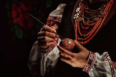Paskalya yumurtasına geleneksel orisim çizen Ukraynalı kadın: Pysanka. Ulusal kostümle çalışan bir sanatçı. Hıristiyan bayramı için hazırlık. 