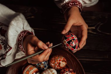 Paskalya yumurtasına geleneksel orisim çizen Ukraynalı kadın: Pysanka. Ulusal kostümle çalışan bir sanatçı. Hıristiyan bayramı için hazırlık. 