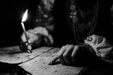 Ukraynalı kadın İncil 'i okuyor. Mum ışığı altındaki kağıt sayfaya odaklanmış. Kyiv Rus tarihi. Mezmur, 19. yüzyıl, dualar ve ilahiler..